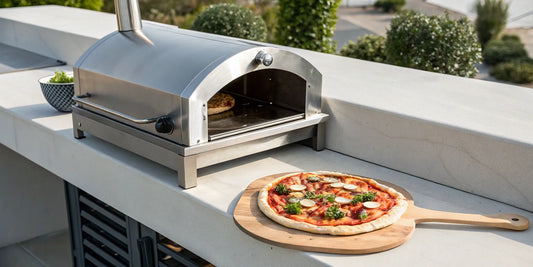 A gas pizza oven on an outdoor counter with a fresh pizza on a wooden peel.
